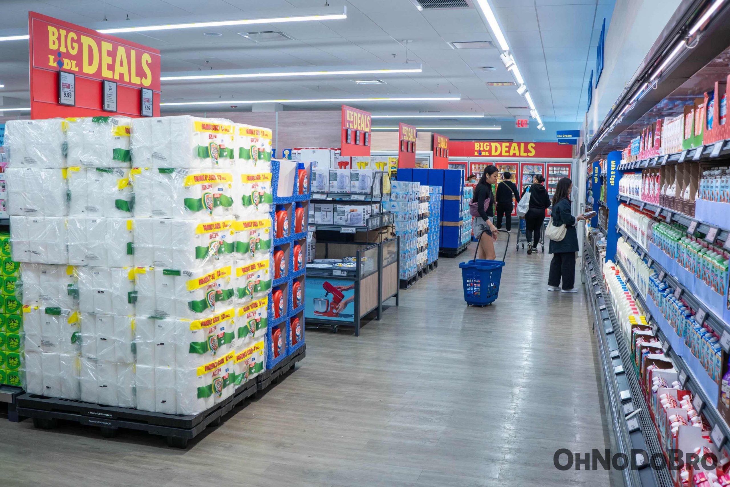 Back aisle of Lidl grocery store. Milk to the right and paper towels on an end cap on the left. Lots of signs for Big Deals